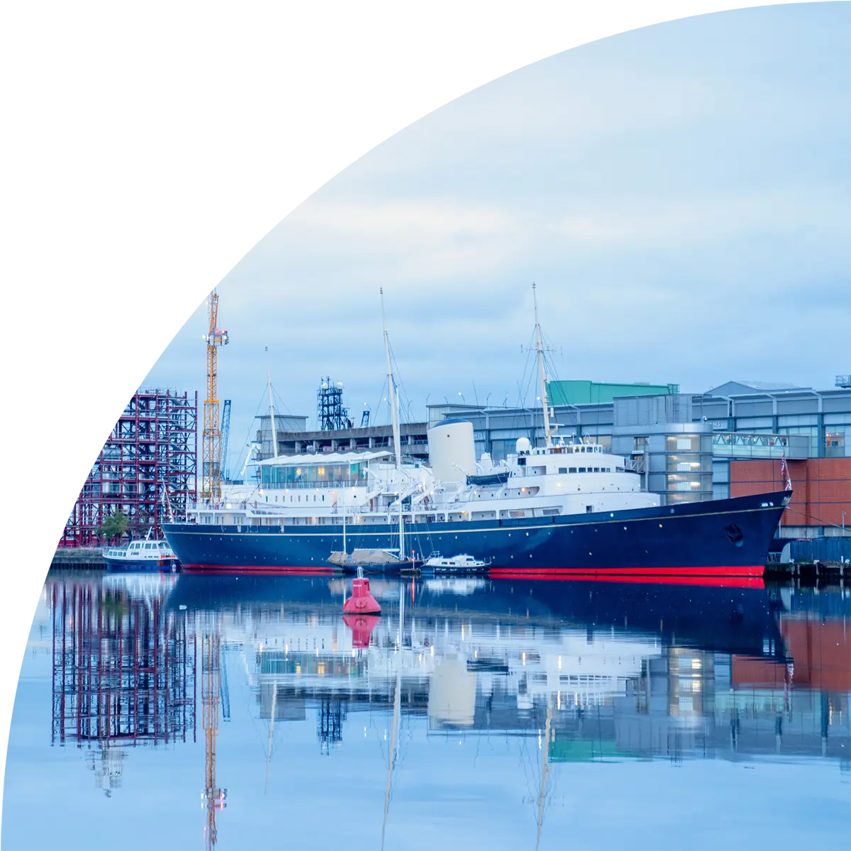 Large blue and white passenger ship docked at an industrial harbor with calm water reflections