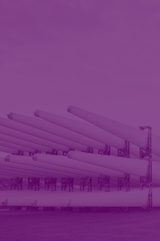 Large white wind turbine blades stacked horizontally in blue racks at a storage facility under overcast sky